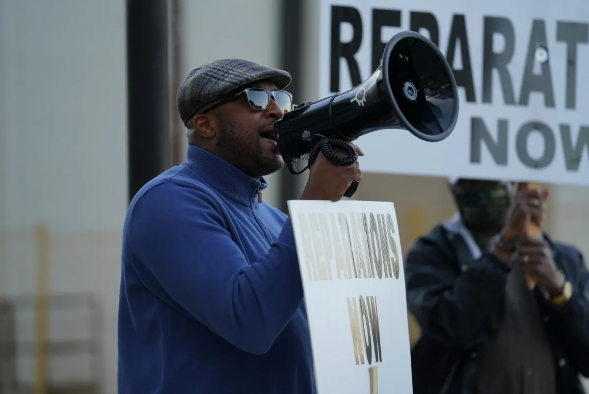 A Black man, wearing a blue polar fleece, leads a protest calling for reparations for victims of the 1921 Tulsa Massacre.