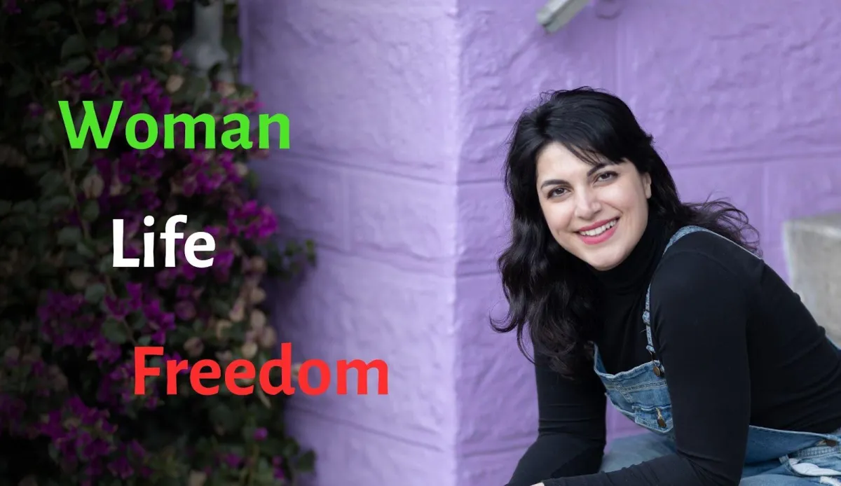 Headshot of a young white woman with long black hair and a black top in front of a purple wall. On the left side of the picture, we see Woman (in green), Life (in white), and Freedom (in red).