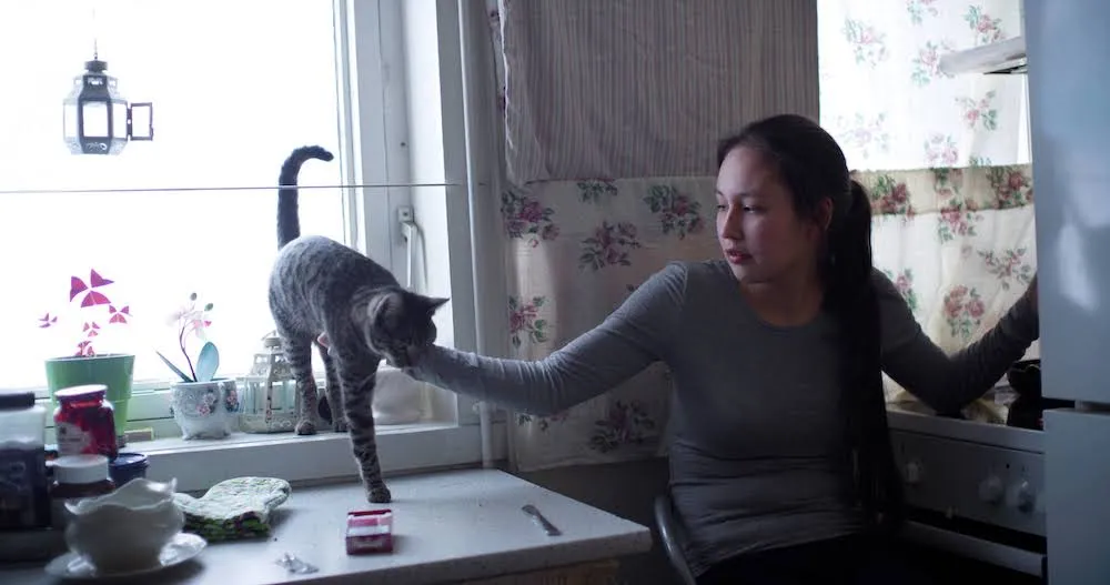 Kirsten Kleist Petersen is a young woman wearing a gray shirt. She is sitting on a chair by a window and petting her cat. From Sidse Torstholm Larsen and Sturla Pilskog’s ‘Winter’s Yearning.’ Courtesy of 'POV.' 