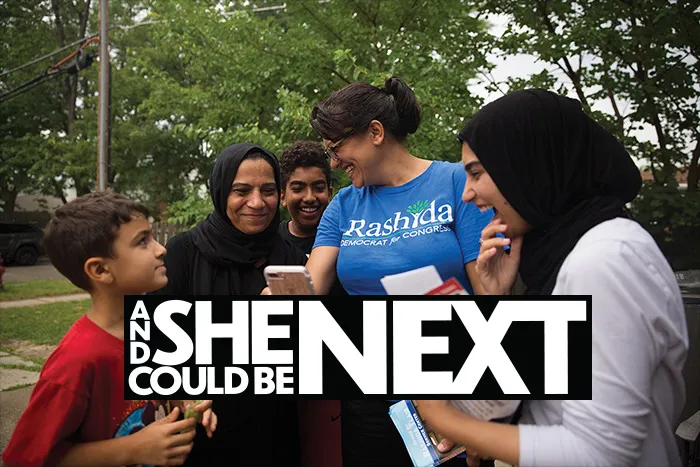 Congresswoman Rashida Tlaib in a blue tshirt on her campaign, surrounded by a family of Muslim supporters