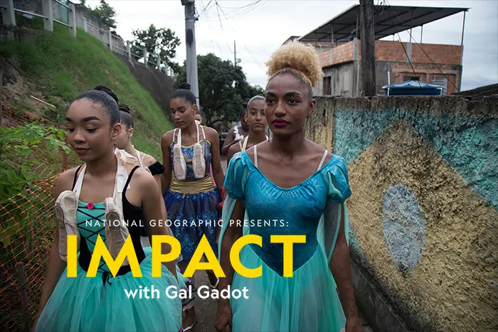 A group of medium- and dark-skinned dancers are walking through an alley on a hill in their performance outfits