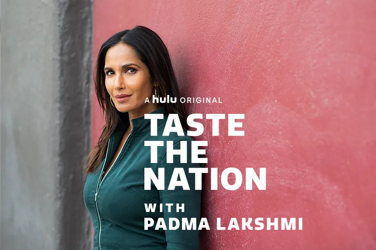 Padma Lakshmi is an Indian woman with straight dark brown hair, wearing a pine green denim jacket, standing against a pink wall