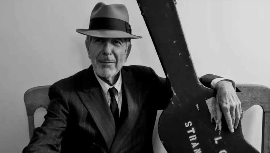 An image from Hallelujah: Leonard Cohen, A Journey, A Song, Leonard Cohen is wearing a fedora and holding a guitar in a black & white photo. 