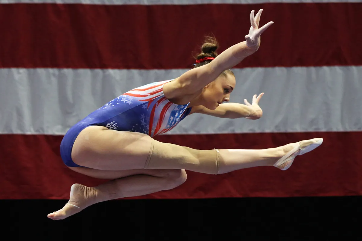 A gymnast in the middle of a routine, A large US flag is behind her