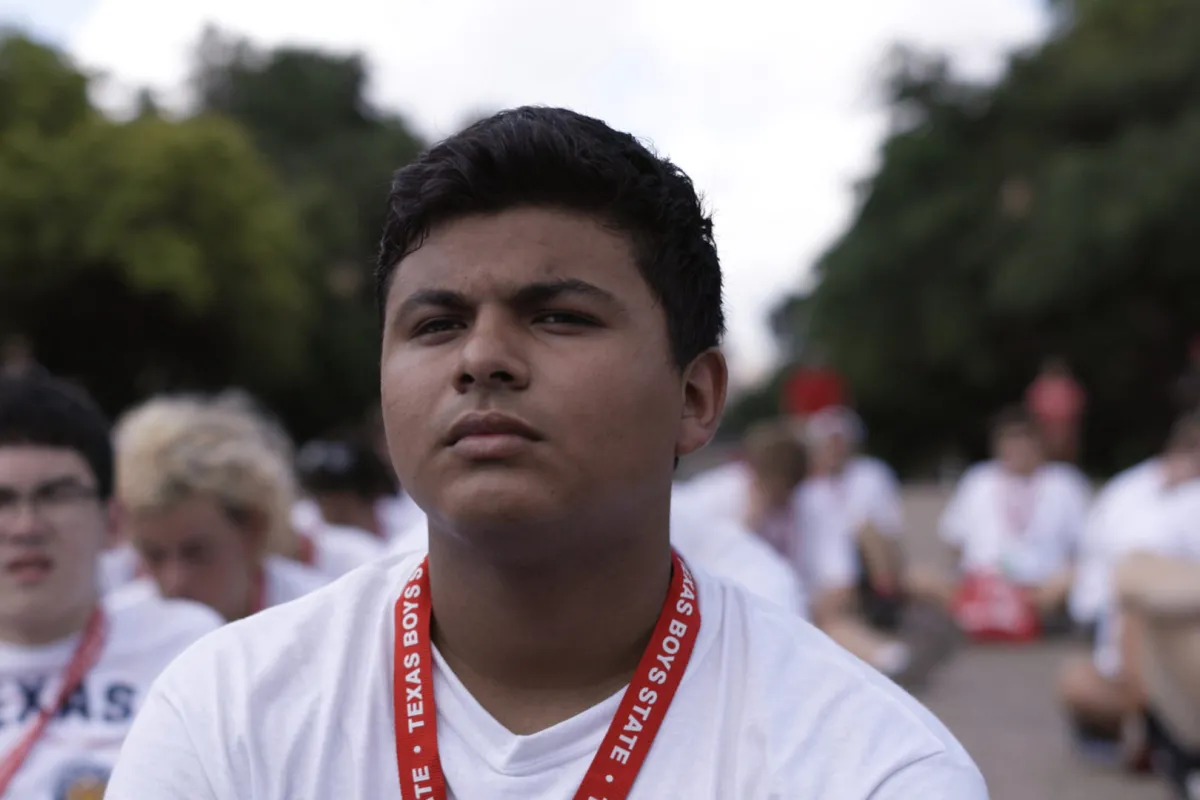 A dark skin-toned teenage boy in white tshirt, wearing red lanyard
