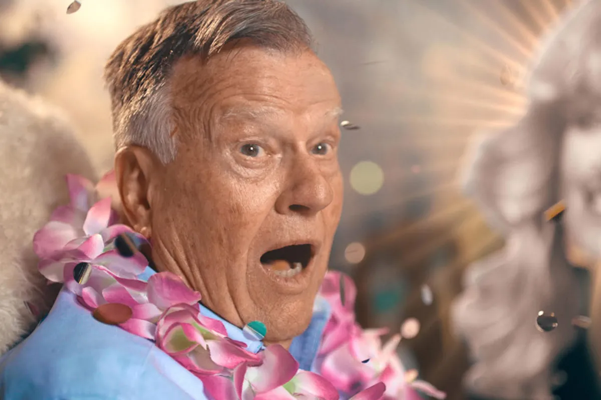 An elderly white man wearing flower leis looking shocked
