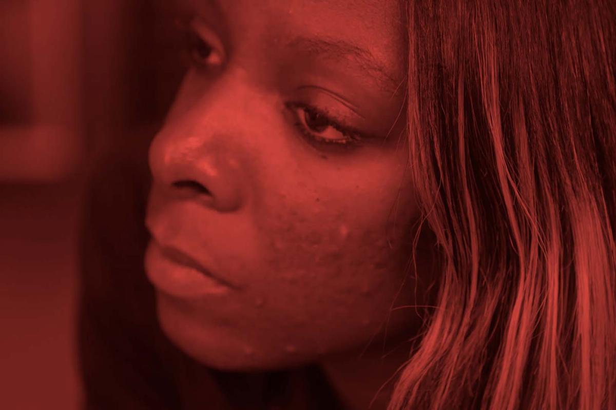 A close up shot of a Black woman with long brown hair looking off screen. A still from 'Woman on the Outside.'