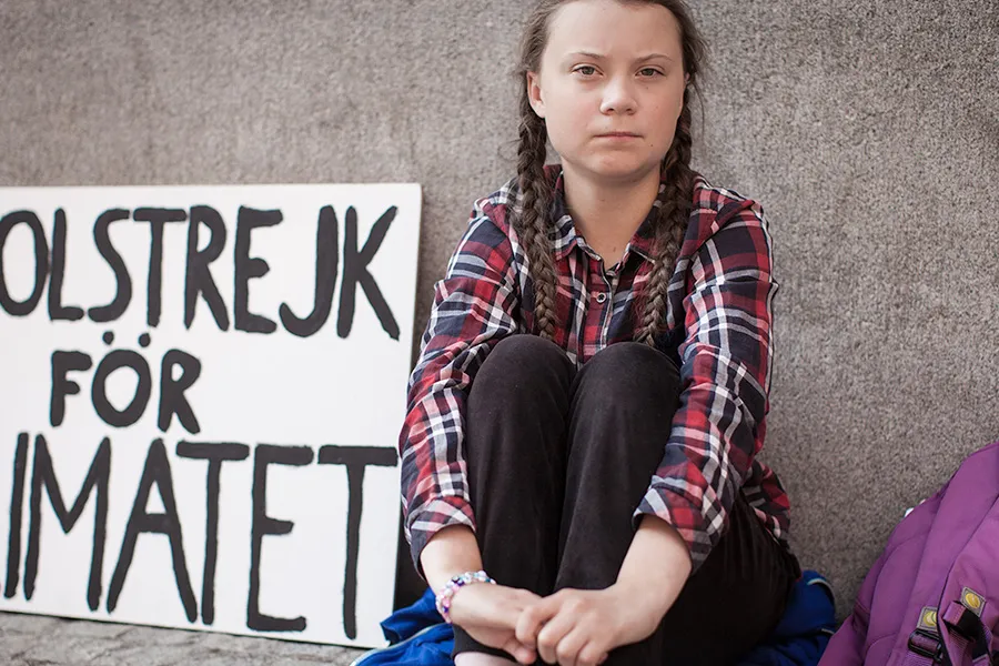 A young teenage girl sitting by a wall with protest sign next to her