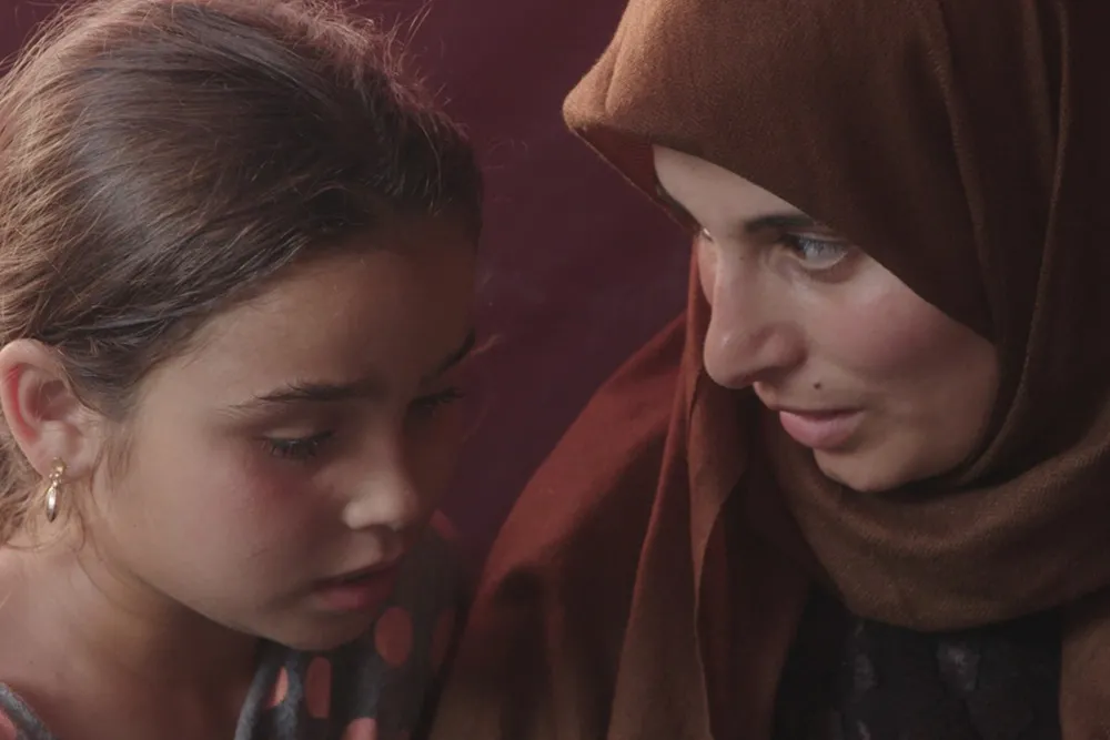 A woman in a brown hijab talks to a little girl.