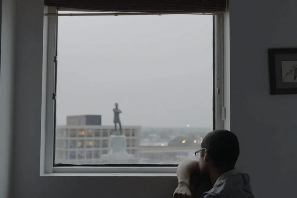 A man stares out the window at a large statue of a person.