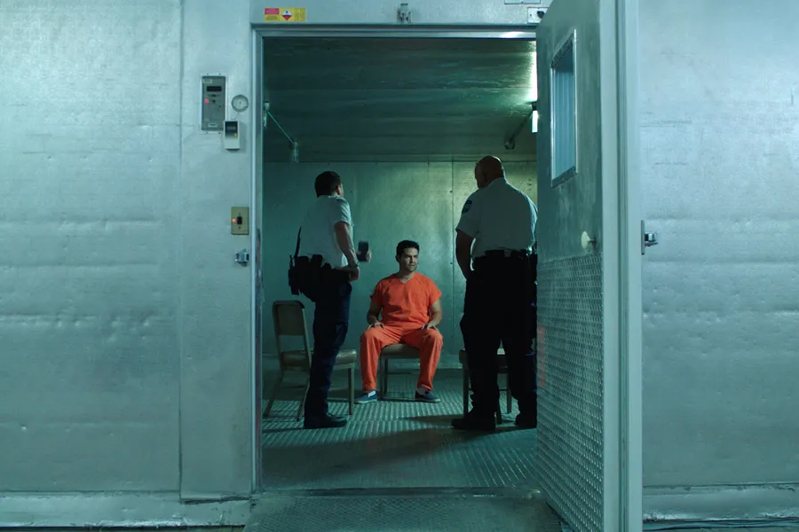 A man in orange jumpsuit is being interrogated by officers