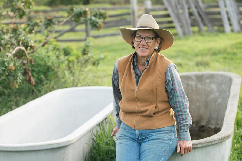 A woman wearing a cowboy hat and vest sitting on a washtub outside in a garden.