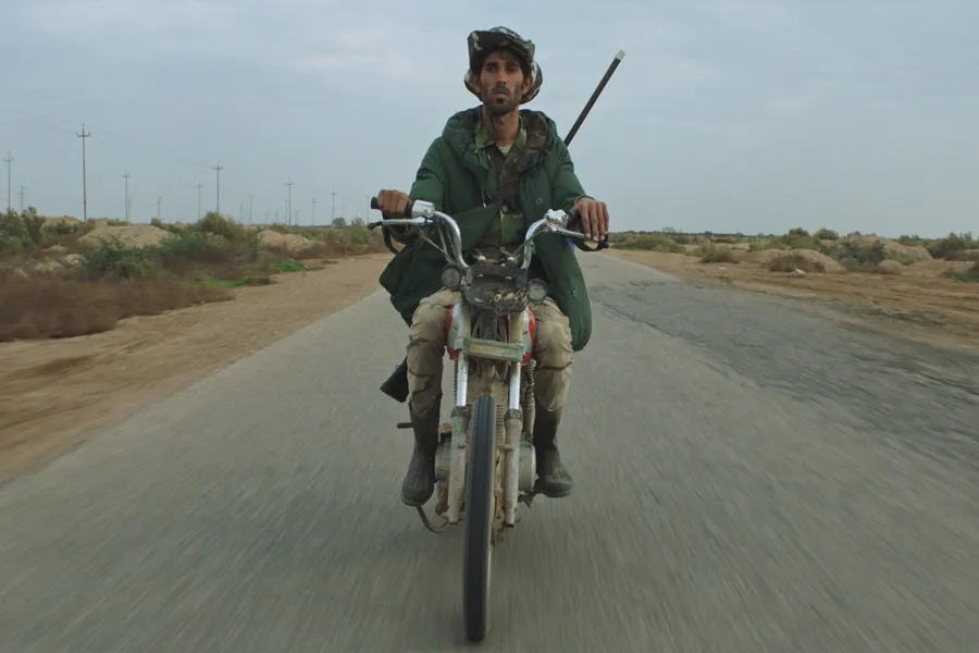 A brown-skin-tonned man in green parka riding a motorcycle