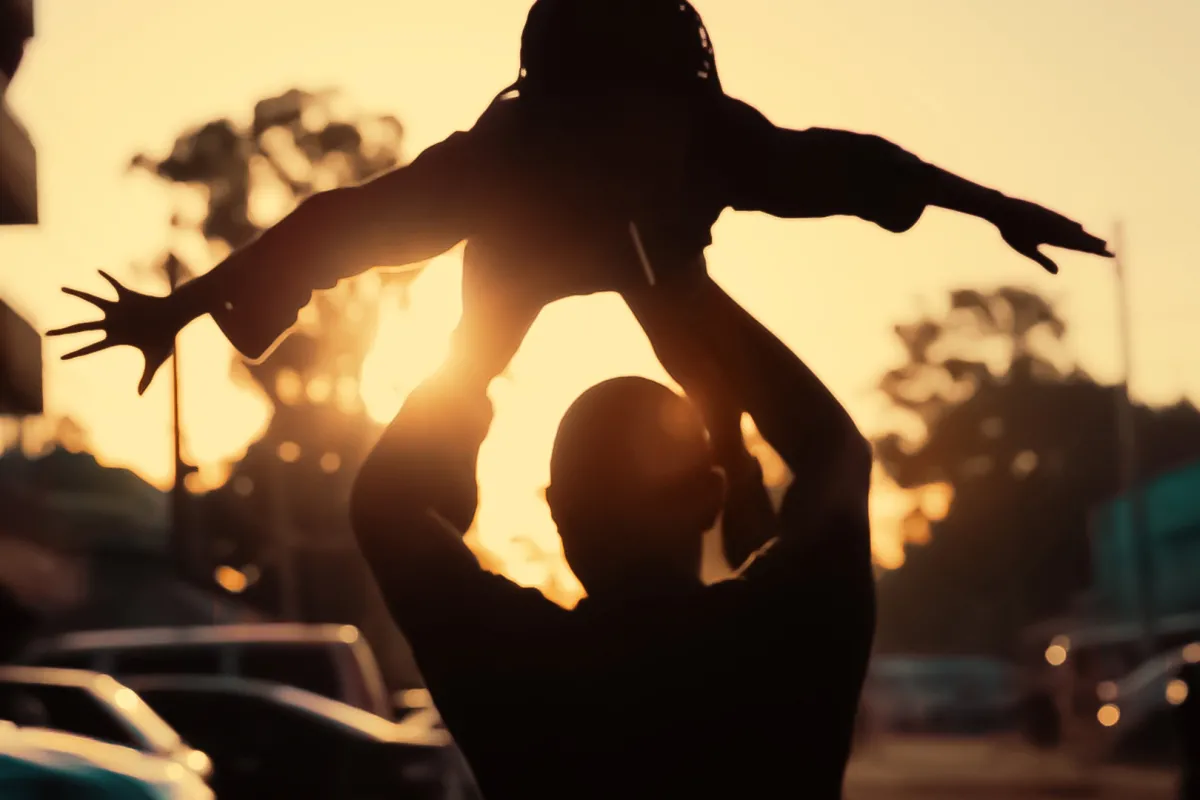 A man is lifting up a child against sunset