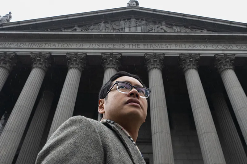 An Asian American man in grey suit in front of the courthouse
