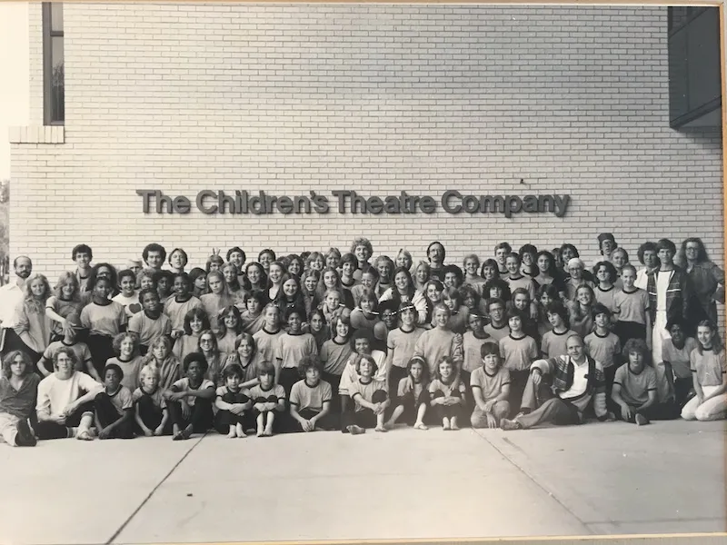 A black and white class photo in front of a building named "The Children's Theater Company"