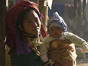 An Asian woman in an elaborate headscarf and necklaces holds her infant child.