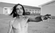 Black and white photograph of a shirtless Native American man reaching his arm out in mid-speech