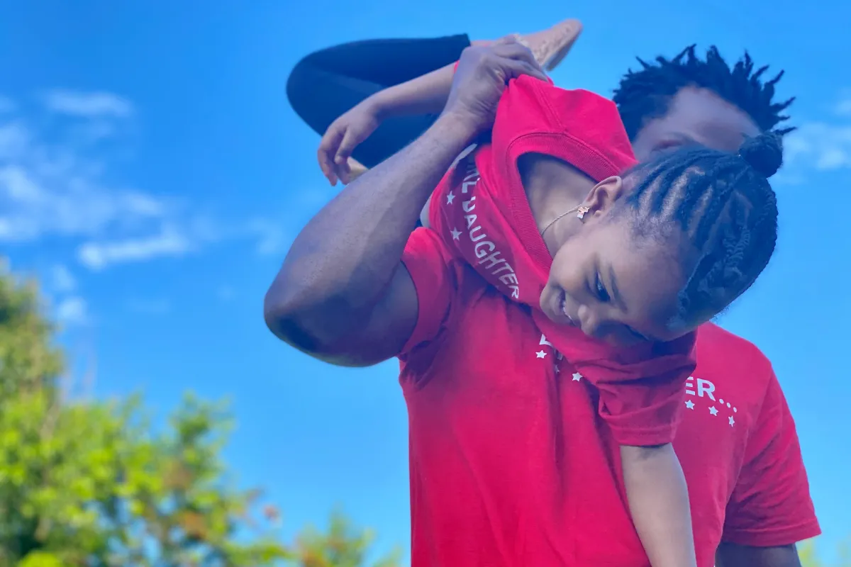 Black father holds smiling child upside down in playful manner