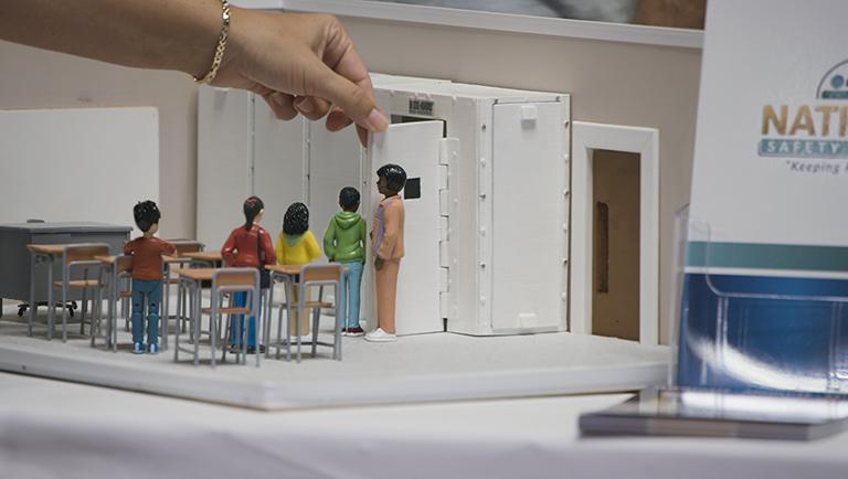 hand of person uses small replica of school classroom to teach gun related safety protocols