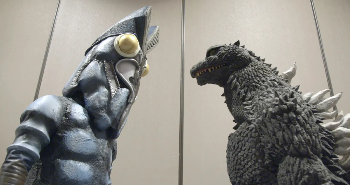 two people in Godzilla costumes stare at each other