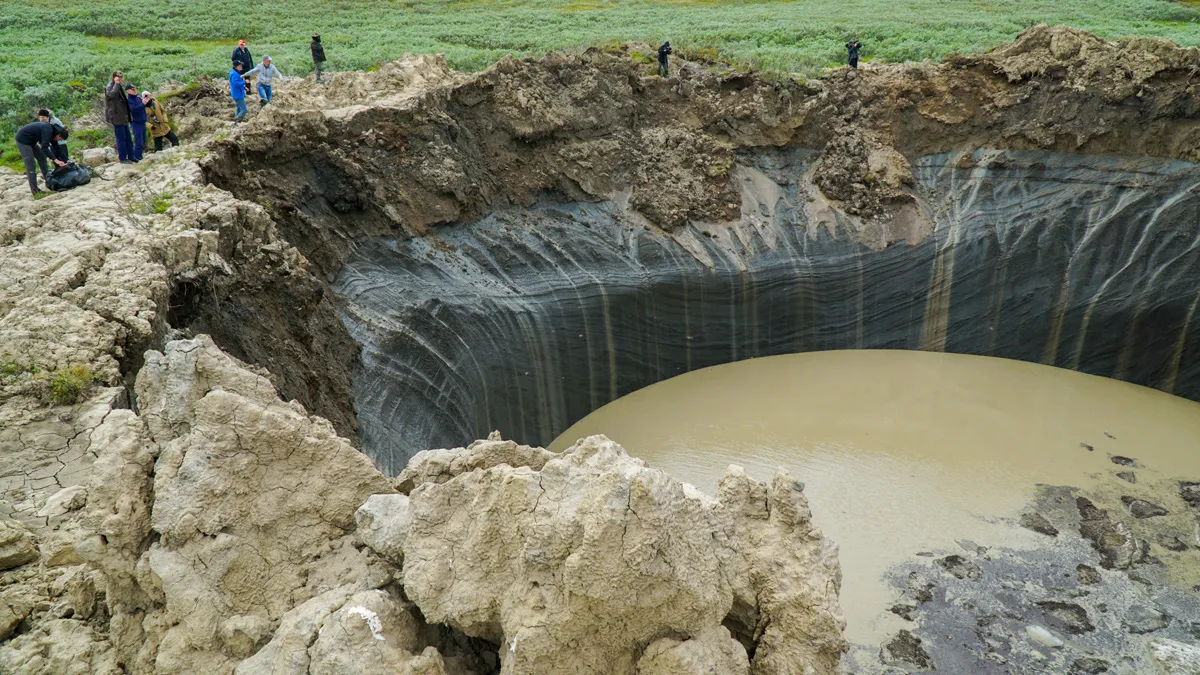 group of people stare into sink hole cause by underground methane explosions