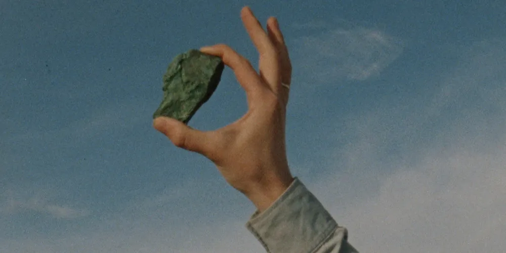 A rock held up to the sky between the index and thumb of a masculine hand