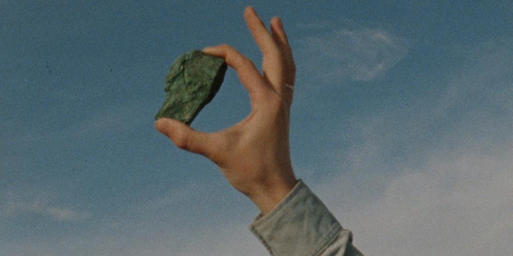 A rock held up to the sky between the index and thumb of a masculine hand