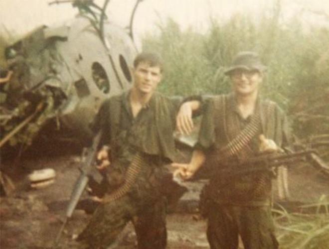 Two soldiers are posing in front of a broken helicopter.
