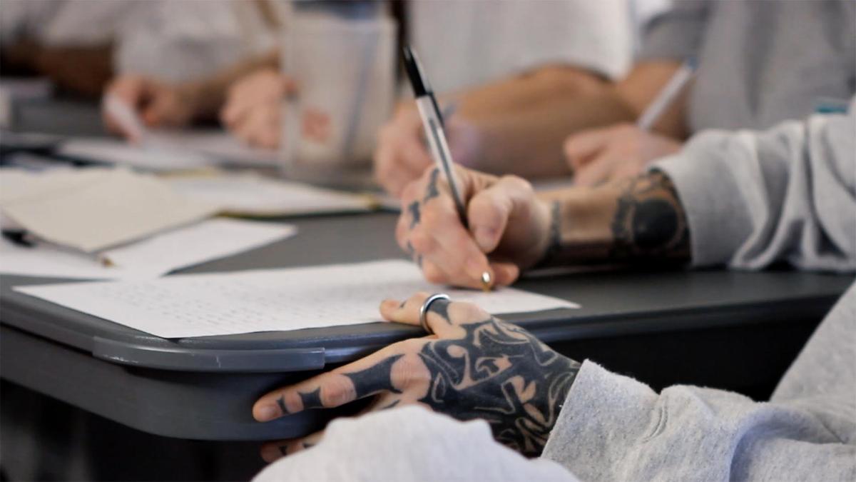 the tattooed hands of an inmate fill out paperwork.