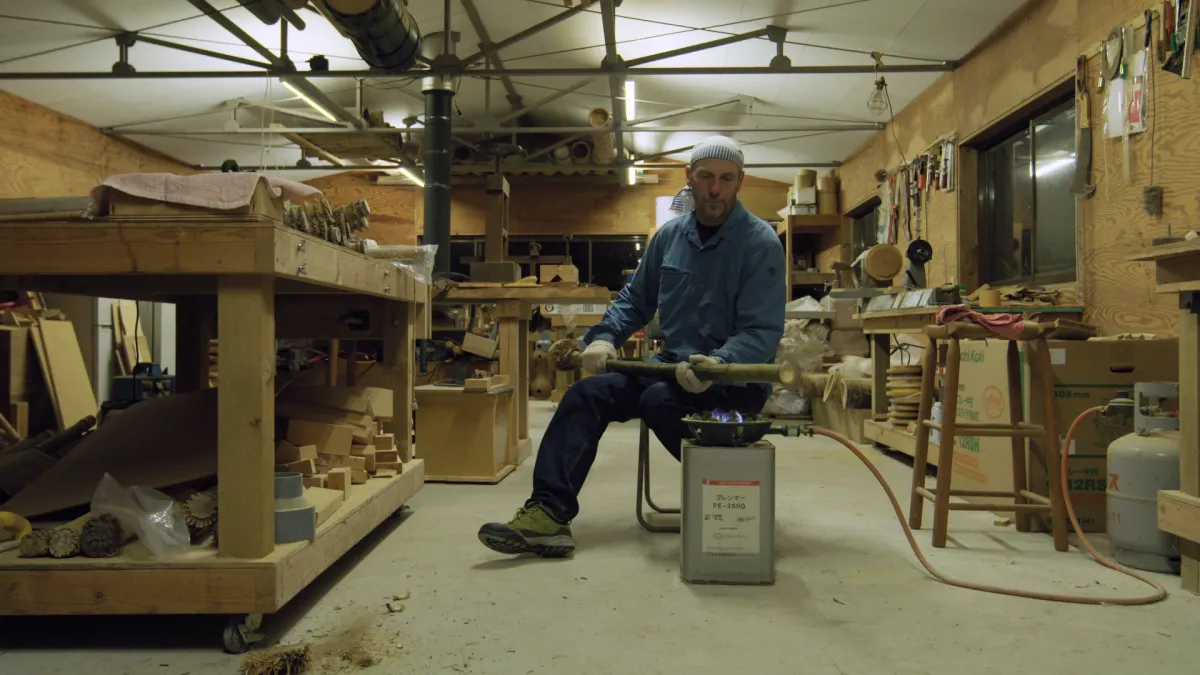 Man sits in a craft workshop with a bamboo flame over a controlled flame.