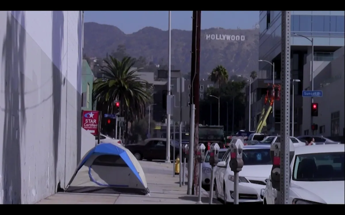 The tent of an unhoused person on the street with the hollywood sign in the background.