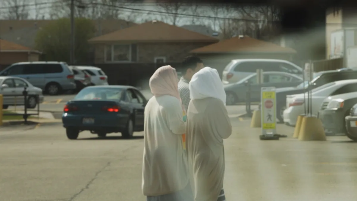 two women dressed in traditional muslim attire walk through parking lot with male 