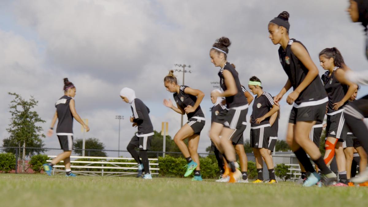 female football team runs laps on a green field in black uniforms