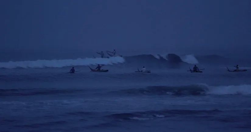 A group of Peruvian fishermen going into the ocean at dawn.