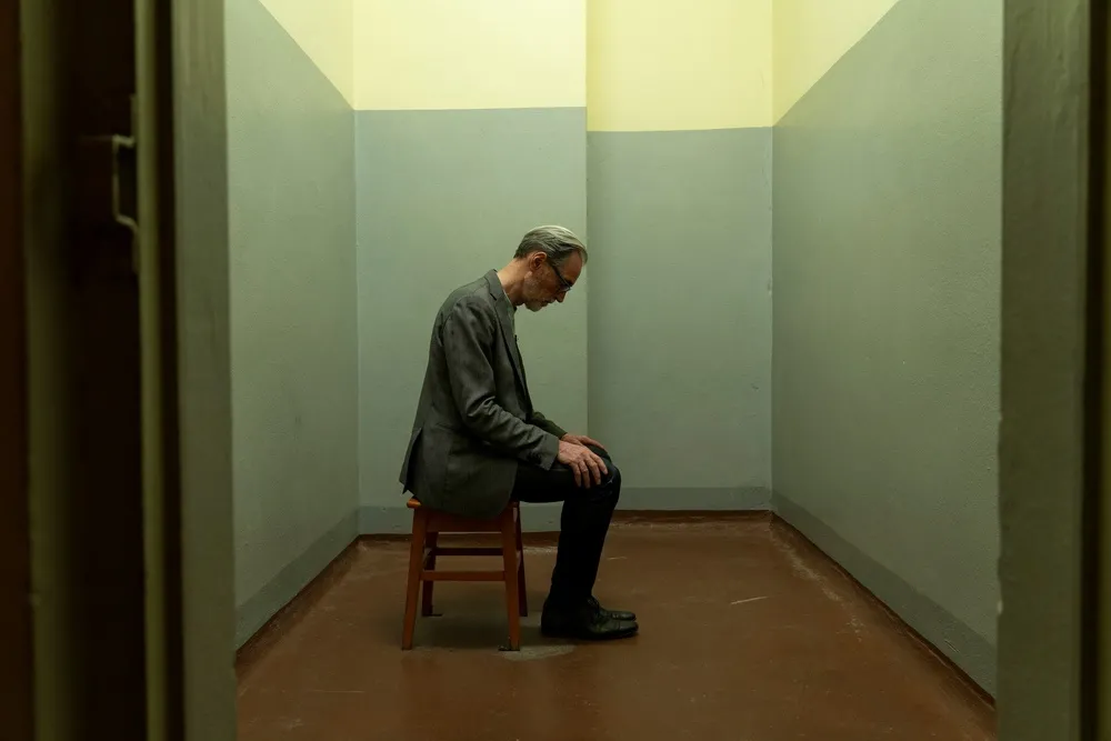 A man sitting in an empty small room looking down at his feet