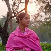 An woman wearing pink stands in nature, the sun setting behind her