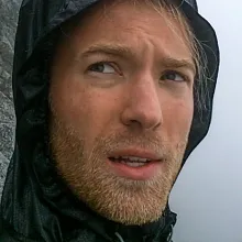 Close-up of a man wearing a windbreaker in front of a cliff