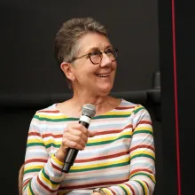 Julia Reichert, a white woman with short grey hair, glasses, and a striped shirt, participates in an on-stage conversation, presented in 2019 by IDA.. Photo: Laura Ahmed