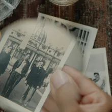 From Victoria Linares Villegas It Runs in the Family. Courtesy of True/False. Hand holding a black and white photo in focus of three people in front of a large statue and building.