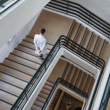 Still from "On the Edge," directed by Nicolas Peduzzi. From overhead, a man in a white doctor's coat descends down a series of stairs.