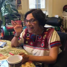 Photograph of Judy Heumann waving at the camera and smiling.