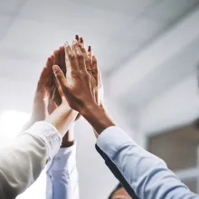 People in a circle. Their hands raised, touching in the center.