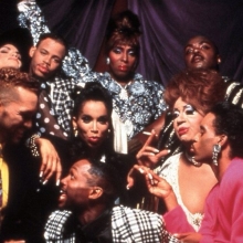 Subjects of the movie Paris is Burning, posing for the camera. They are all in glamorous makeup and fashion and colorful clothing.