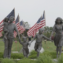 Still from 'Richland' depicting a statue of a family walking proudly in front of two columns of American flags, which border a series of manicured lawns. Photo credit: Helki Frantzen