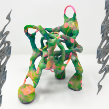 An art piece by Nat Decker: on the left and right edges of a green, pink, and orange twisted 3D sculpture that looks like it’s made of clay we see 3D iridescent dark grey chrome squiggles