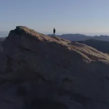 Blue skies and mountains with a person standing alone on one mountain.