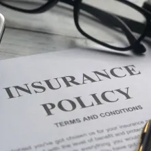 An image with a letter that reads Insurance Policy on top of a desk with glasses and a calculator