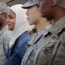 A Muslim woman wearing a hijab stands among a line of people in military uniforms