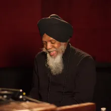 A man with a long beard, wearing dark attire and a turban, playing an organ